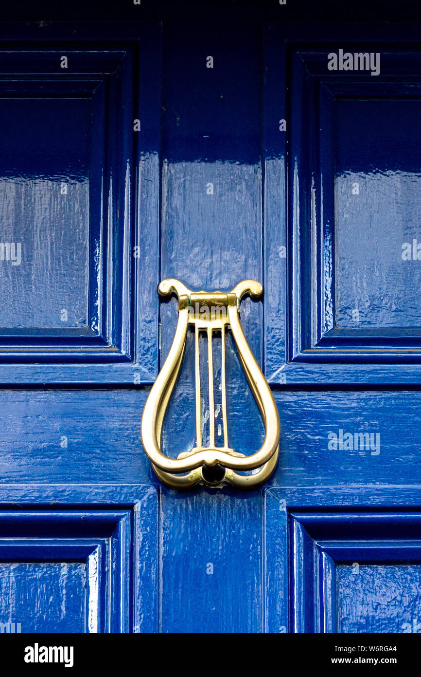 Heurtoir de porte d'or sous la forme d'une harpe irlandaise sur un porte en bois bleu foncé Banque D'Images