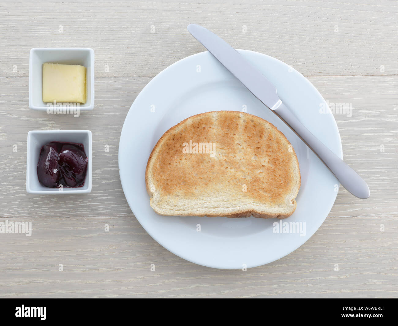 Une assiette petit-déjeuner toast beurre confiture couteaux jelly sur table en bois Banque D'Images