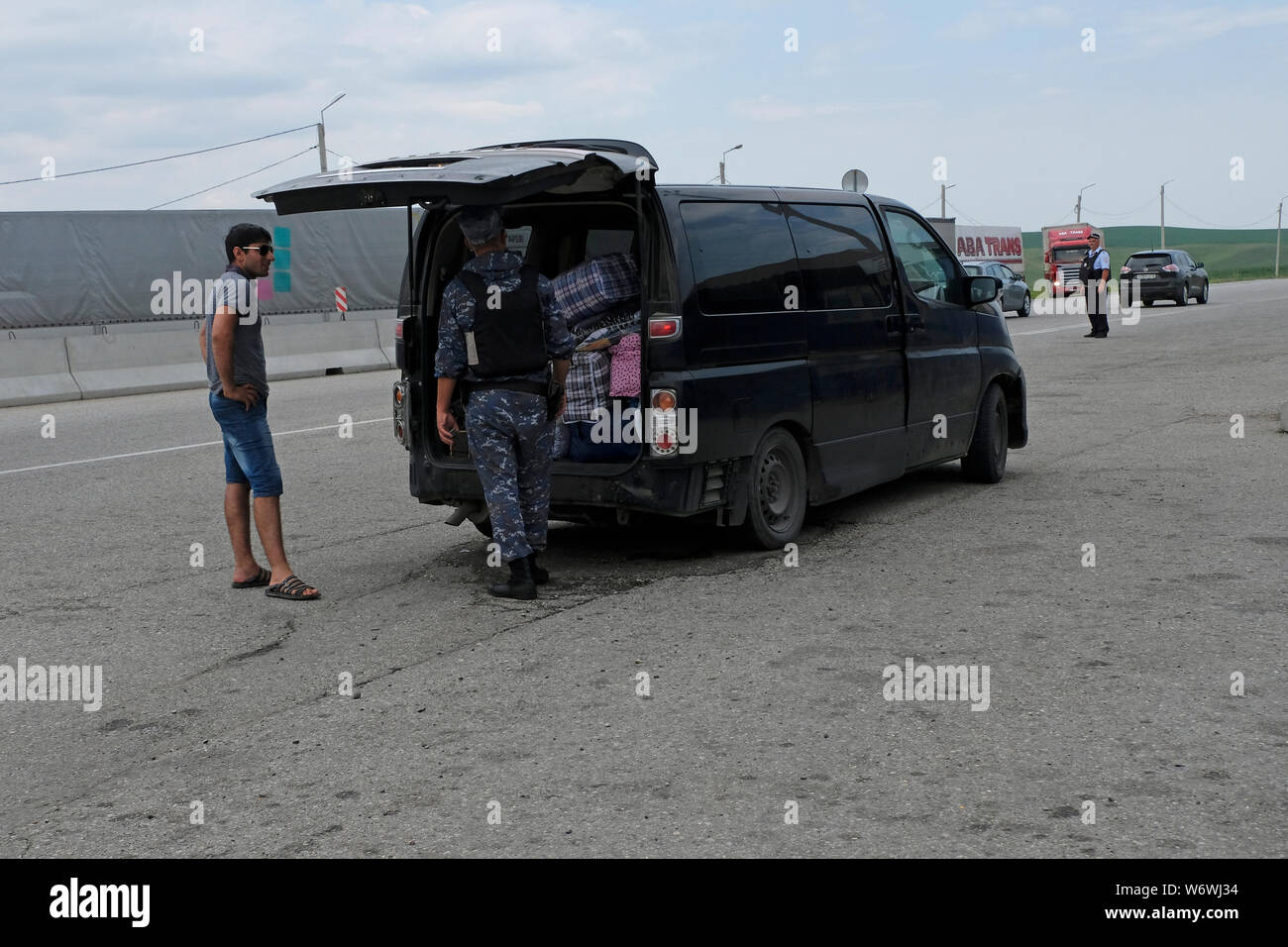Un policier le port de gilet pare-balles vérifie le coffre d'un véhicule pour des armes de contrebande et de l'alcool à Malka contrôle à la frontière entre krai de Stavropol et Kabardino-Balkar en République du Caucase du Nord le District fédéral de la Russie. Banque D'Images