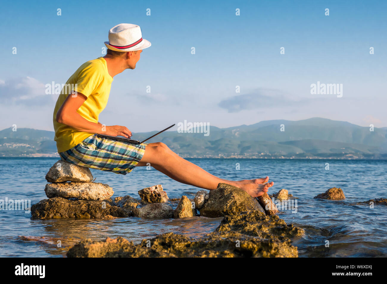 Jeune hipster en utilisant un ordinateur portable, concept de touriste. Man working on laptop computer in exotiques tropicales de l'océan. Connexion Internet 3G, 4G. Bureau virtuel. Les voyages et le travail. Homme travaille sur mer Banque D'Images