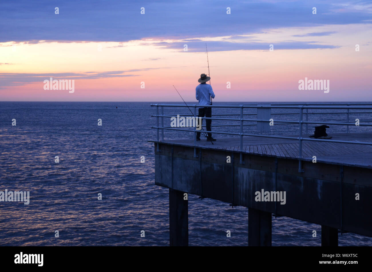 PRISE le matin : un homme prend un peu de pêche le matin juste avant le lever du soleil sur une jetée au large de la baie d'Absecon dans la ville de l'Atlantique, New Jersey. Banque D'Images