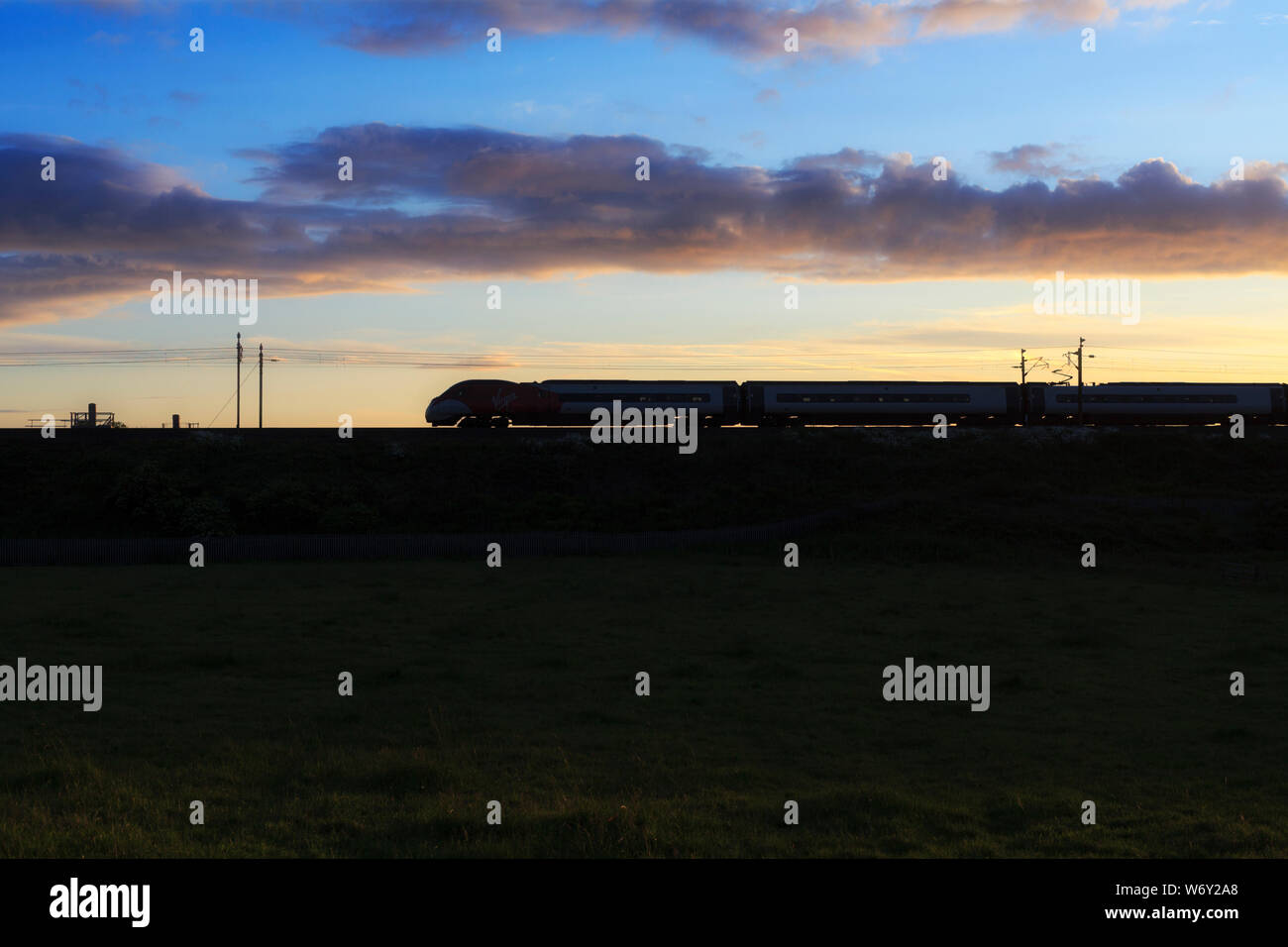 La côte ouest Virgin Trains pendolino sur la ligne principale de la côte ouest au coucher du soleil faire une silhouette Banque D'Images