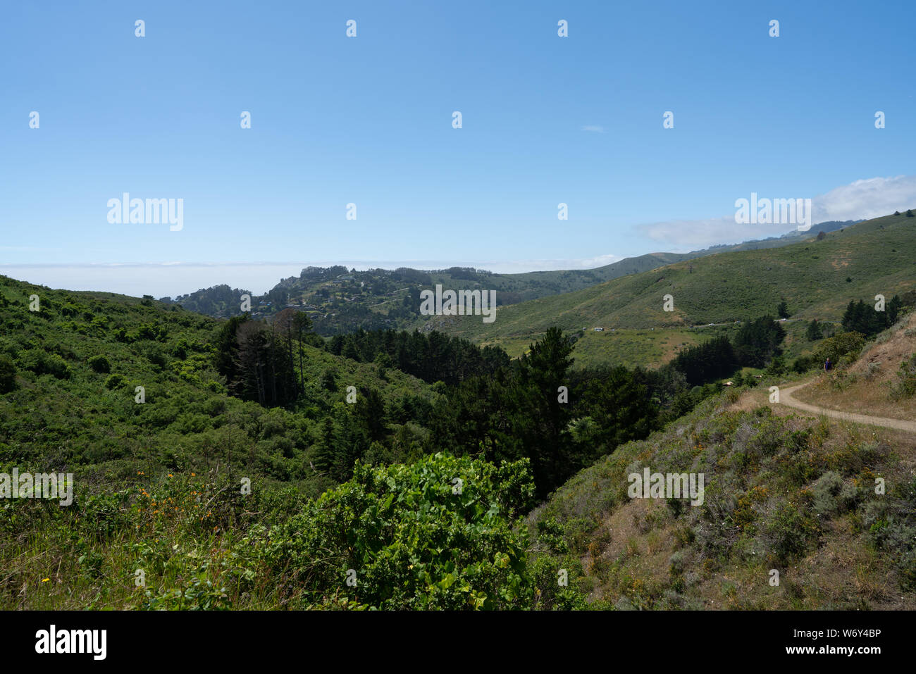 Un ciel bleu, des collines herbeuses, l'homme sur un chemin de randonnée, ville en arrière-plan Banque D'Images