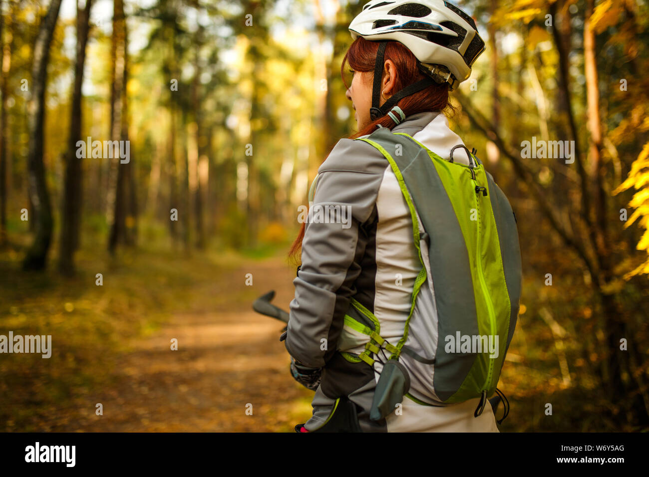 Photo de smiling woman wearing helmet et vêtements de sport à bicyclette en forêt d'automne Banque D'Images