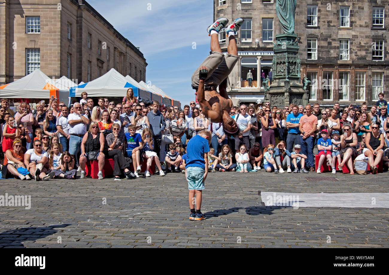Parliament Square, Édimbourg, Écosse. 3 août 2019. Edinburgh Fringe performers, American breakdance Jose Angel Colon Jr culbutes sur une brave jeune volontaire pendant qu'un autre membre de l'équipe Christopher Cuba Munoz culbutes et écumage plus de 4 bénévoles de l'auditoire. Banque D'Images
