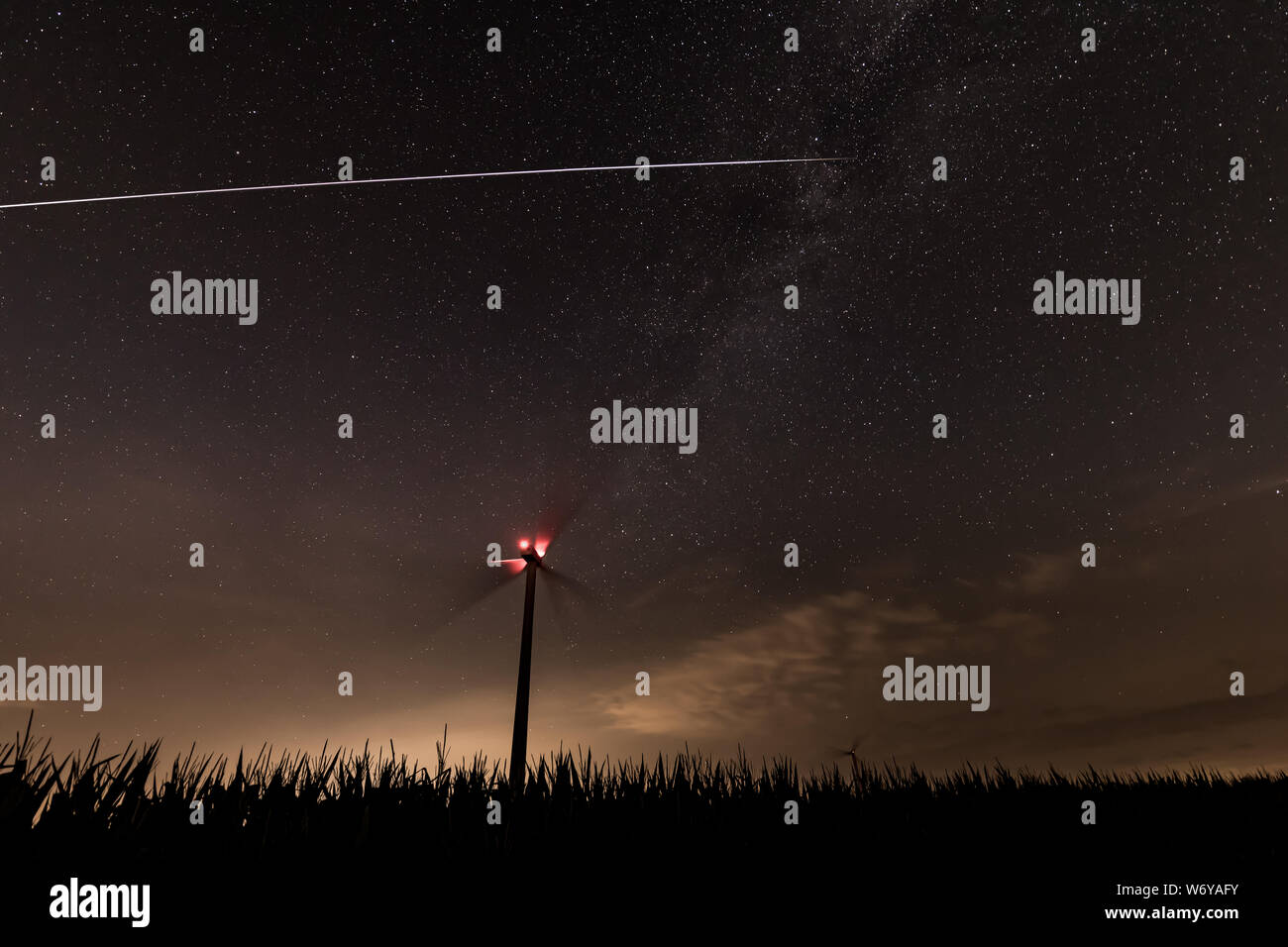 Station spatiale internationale éclairée par le soleil est visible par une nuit étoilée survolant une éolienne dans un champ Banque D'Images