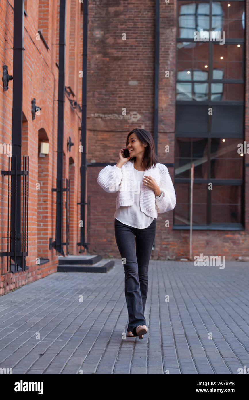 Belle asiatique fille heureuse marche dans la rue et de parler sur téléphone mobile. Modèle est souriant,Longueur totale Banque D'Images