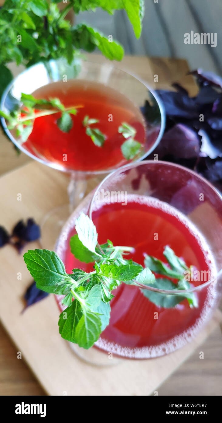 Vue de dessus de deux verres avec un cocktail rafraîchissant rouge décoré de feuilles de menthe sur fond de bouquets de menthe et basilic pourpre, selective focus Banque D'Images