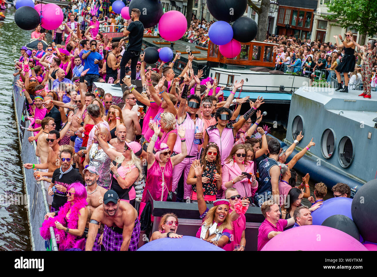 Un groupe de personnes et Drag Queens sont vus sur un bateau portant des vêtements tout en rose et violet holding balloons pendant la parade.Le Canal Parade est ce qu'Amsterdam Gay Pride est célèbre pour. C'est la couronne sur leurs deux semaines du festival durable que propose plus de 200 événements. Les bateaux commencent à la scheepvaart Museum à la partie est du centre-ville vers la rivière Amstel. Les flotteurs continuer à partir de là prendre le Prinsengracht vers la Westerdok. Le canal Parade commence autour de 12h30 et prend tout l'après-midi. Environ 80 bateaux de différentes organisations internationales et organisations à but non lucratif Banque D'Images