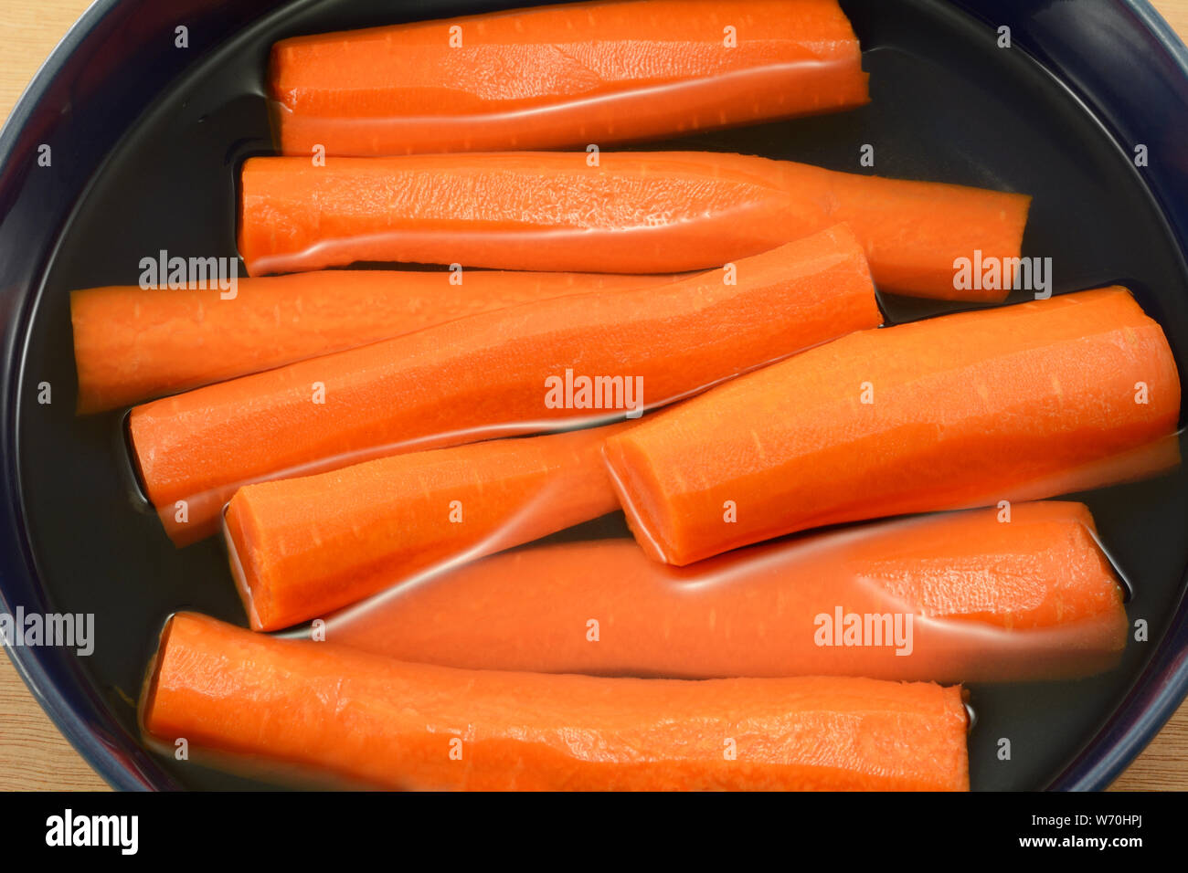 Carottes pelées et coupées en deux dans le bol d'eau fraîche pour garder frais et croquant dans réfrigérateur Banque D'Images