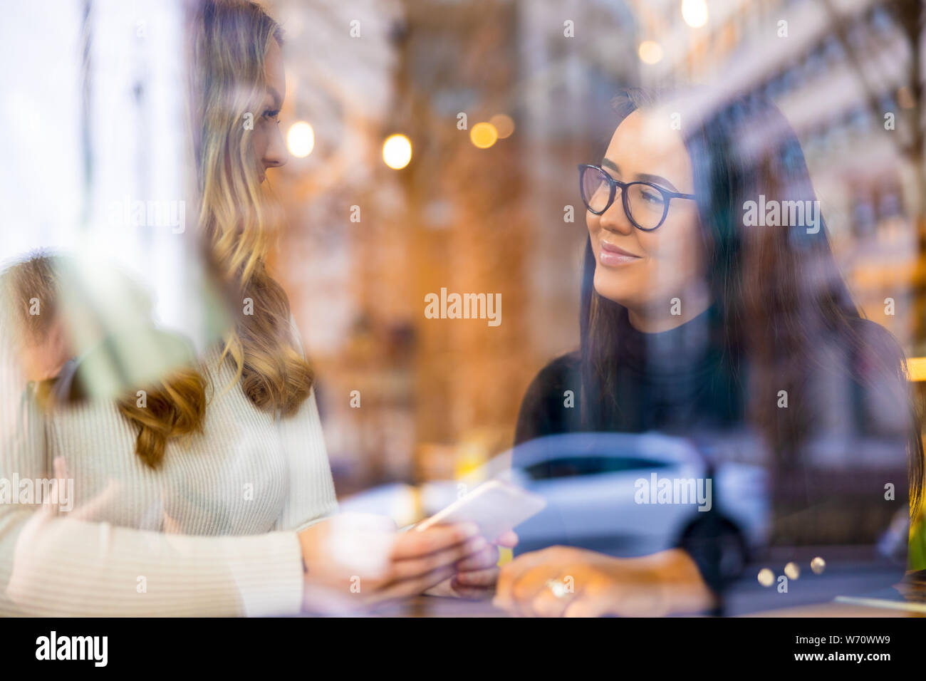 Deux jeunes femmes parlant au café en ville vue par la fenêtre Banque D'Images