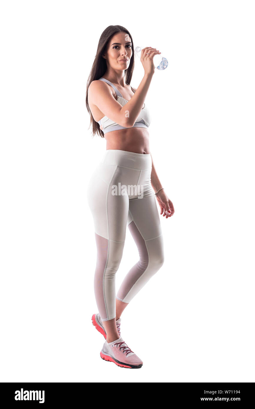 Femme de remise en forme de l'eau potable et la bouteille rafraîchissante après entraînement looking at camera. Corps plein isolé sur fond blanc. Banque D'Images