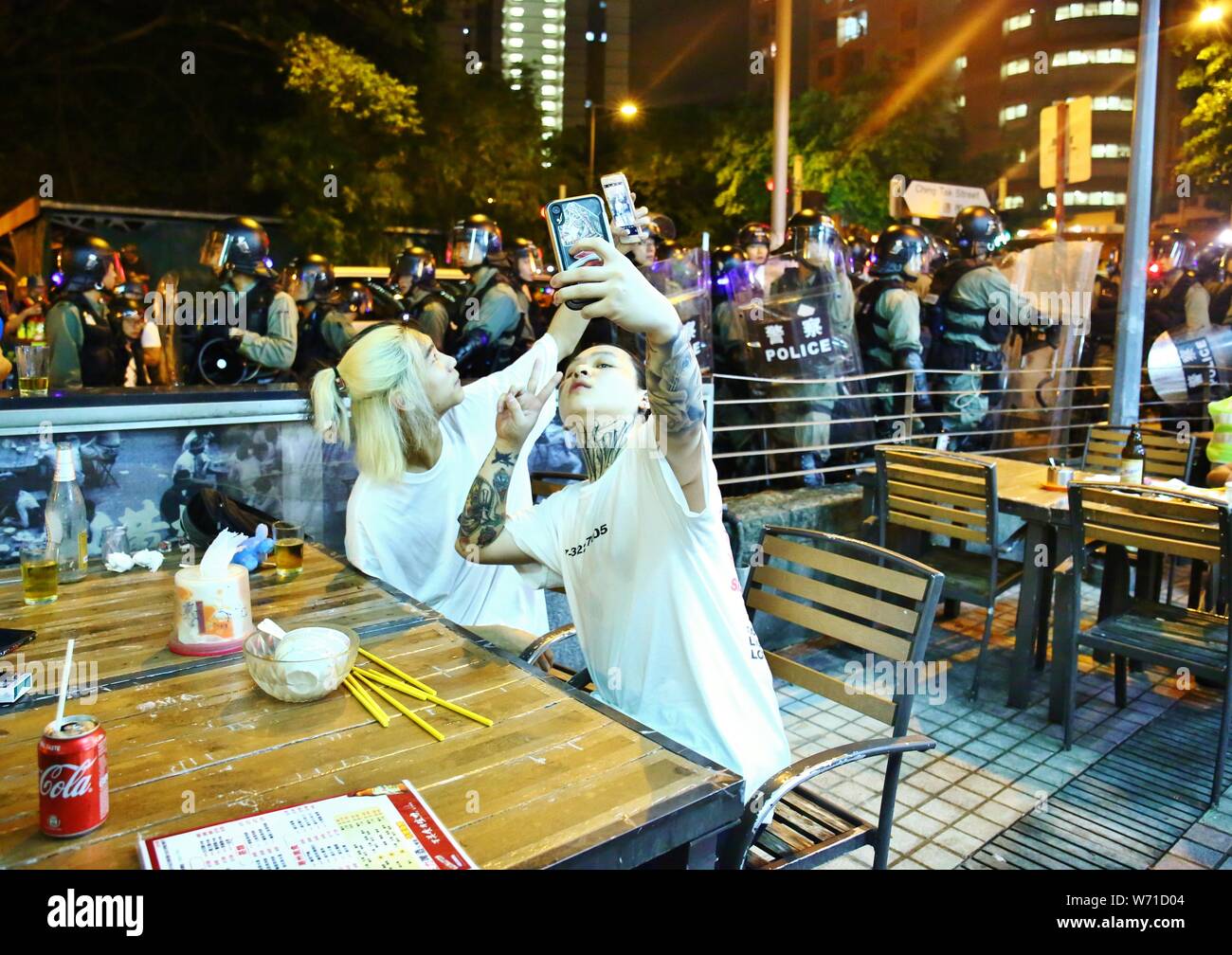 Hong Kong, Chine. 4e août 2019. Déployer la police des gaz lacrymogènes sur les zones résidentielles à disperser la foule lorsque les manifestants entourent la station de police de Wong Tai Sin et l'appel à la libération des manifestants arrêtés. Ici deux résidents locaux prennent des autoportraits tandis que la police anti-émeutes est en marche vers la nuit food derrière eux. Gonzales : Crédit Photo/Alamy Live News Banque D'Images