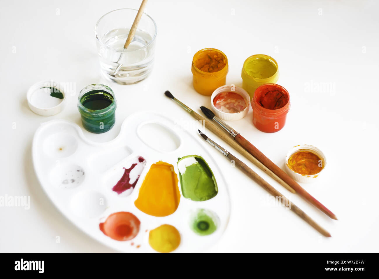 Gouache multi-couleur des peintures, pinceaux, palette et un verre d'eau pour les pinceaux sur un fond blanc Banque D'Images