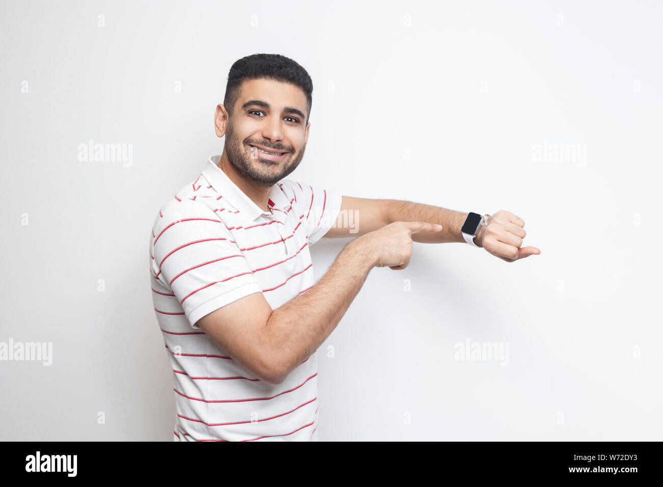 Bon résultat et ontime. Heureux beau jeune homme barbu en t-shirt à rayures, montrant sa permanent smart watch and looking at camera avec sourire à pleines dents. Banque D'Images