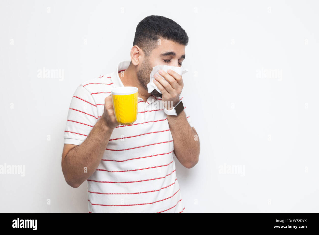Le froid et la grippe. Portrait de jeune homme barbu malade en t-shirt à rayures, permanent, le nettoyage des tissus Holding SA, boisson chaude, essayez d'être traités. Banque D'Images