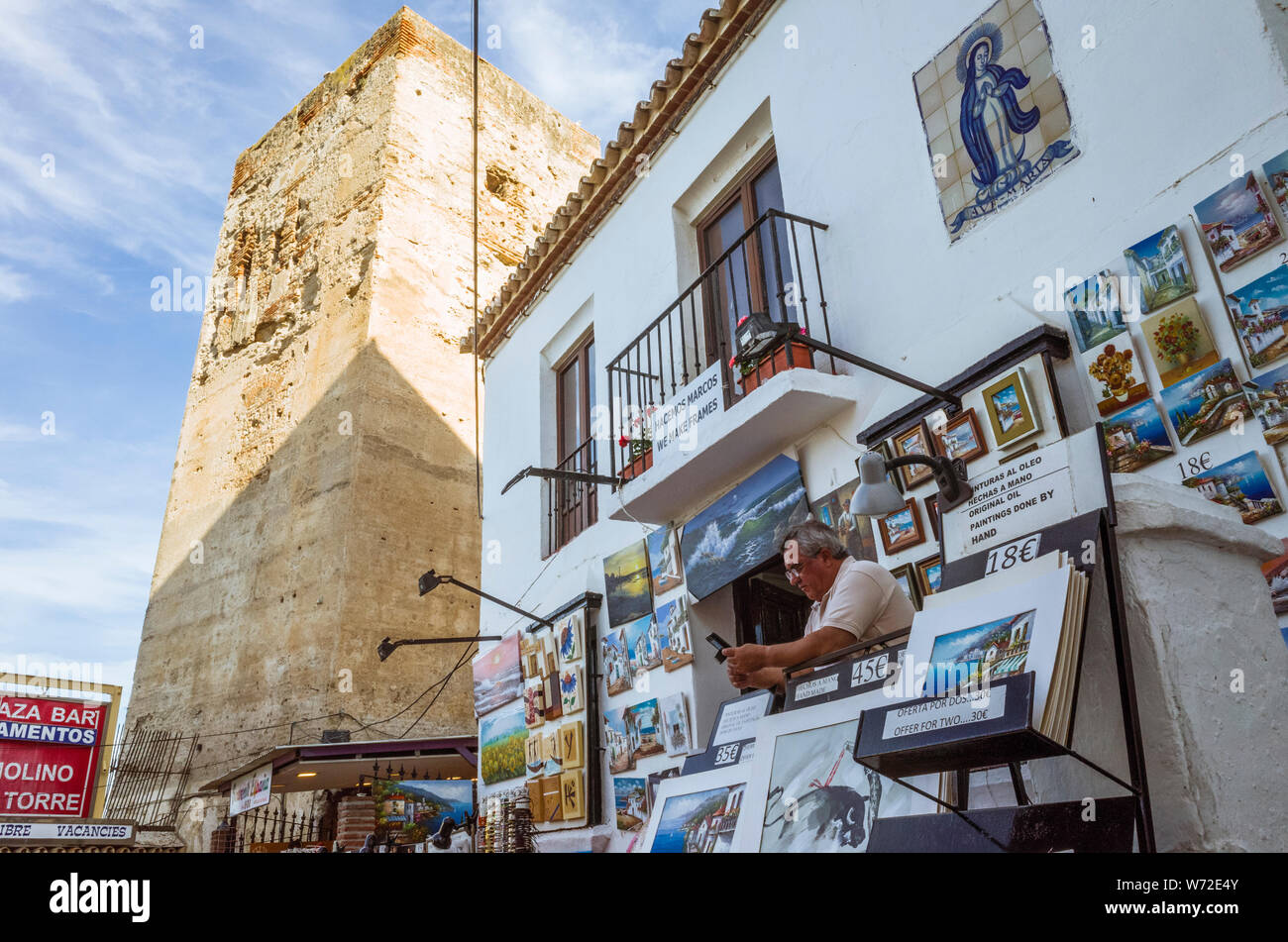 Torremolinos, Malaga province, Andalusia, Spain : Un homme se trouve à l'extérieur d'une boutique par la Torre del Pimentel, également connu sous le nom de Torre de los Molinos. Banque D'Images
