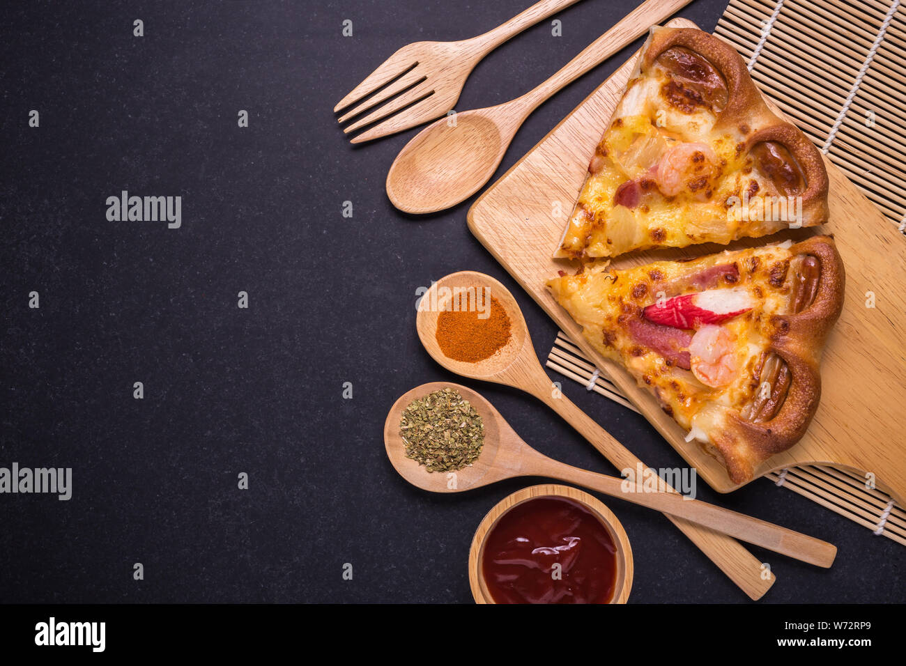 Vue supérieure de la pièce de la pizza sur la plaque en bois et pierre noire fond de table Banque D'Images