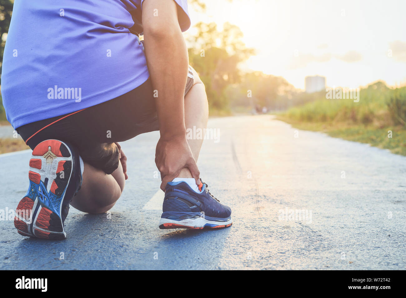 Blessures causées par le concept d'entraînement : asian man utiliser mains tiennent à sa cheville pendant le fonctionnement sur route dans le parc. L'accent sur la cheville. Banque D'Images