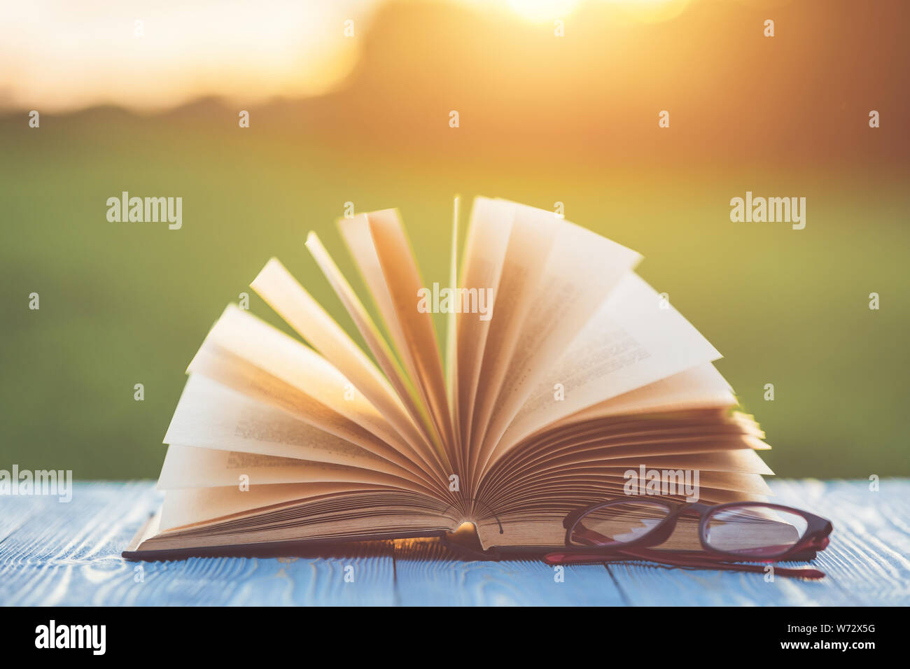 Close up book et lunettes sur table en bois avec abstract blur bokeh et au lever du soleil ou coucher du soleil Banque D'Images
