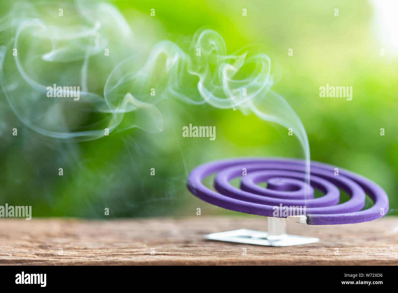 L'insectifuge violet et de la fumée blanche sur table en bois avec éclairage arrière-plan flou vert de l'espace pour le texte, le design, la publicité ou montage photo Banque D'Images