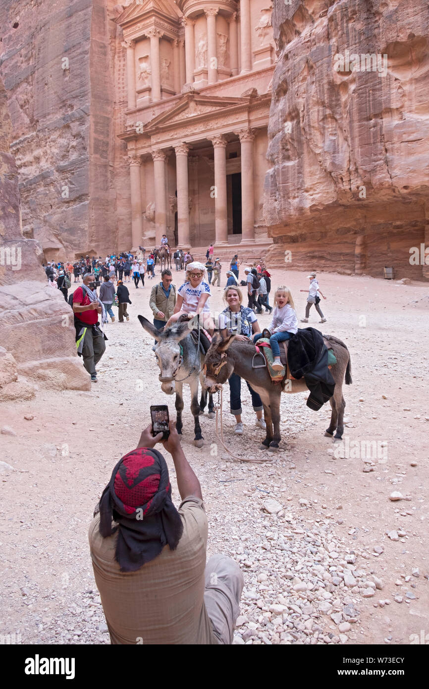 Un groupe de touristes et 2 ânes posent pour une photo devant le Conseil du Trésor, un temple dans la ville antique de Petra en Jordanie. Banque D'Images