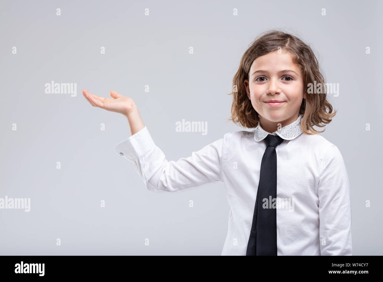 Jeune fille dans l'uniforme scolaire qui fait signe au côté palm vide avec le sourire dans un concept de placement de produit et la publicité sur une zone blanche Banque D'Images