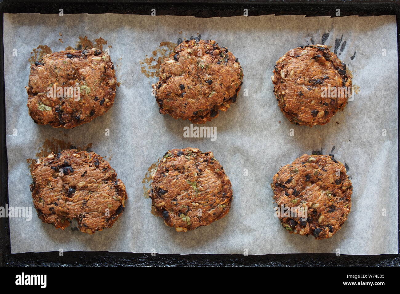 Six haricots noirs vegan burgers sur une plaque recouverte de papier sulfurisé, fraîchement sorti du four. Banque D'Images