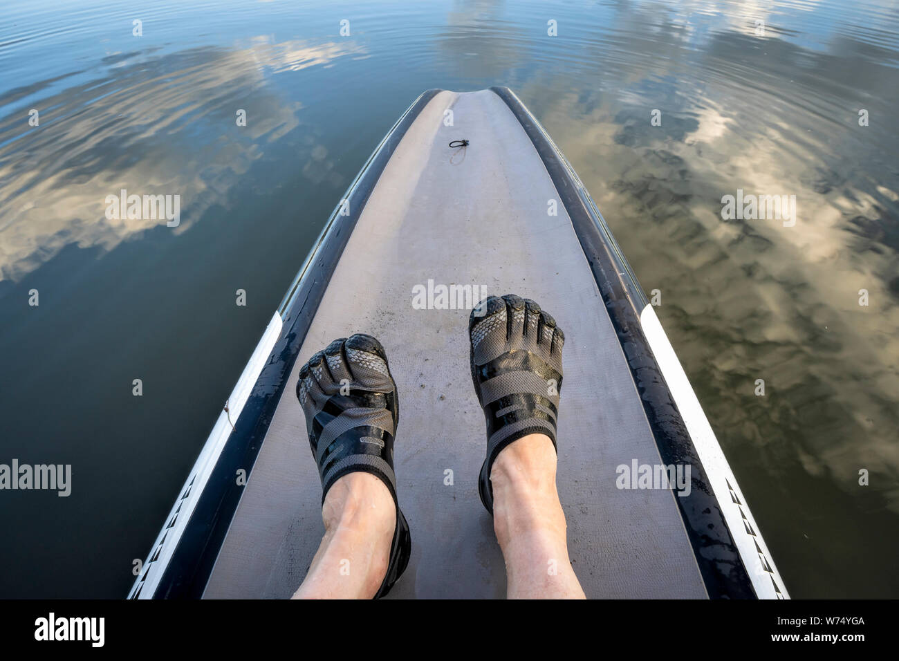 Homme pieds dans l'eau cinq doigts chaussures sur un stand up paddleboard Banque D'Images