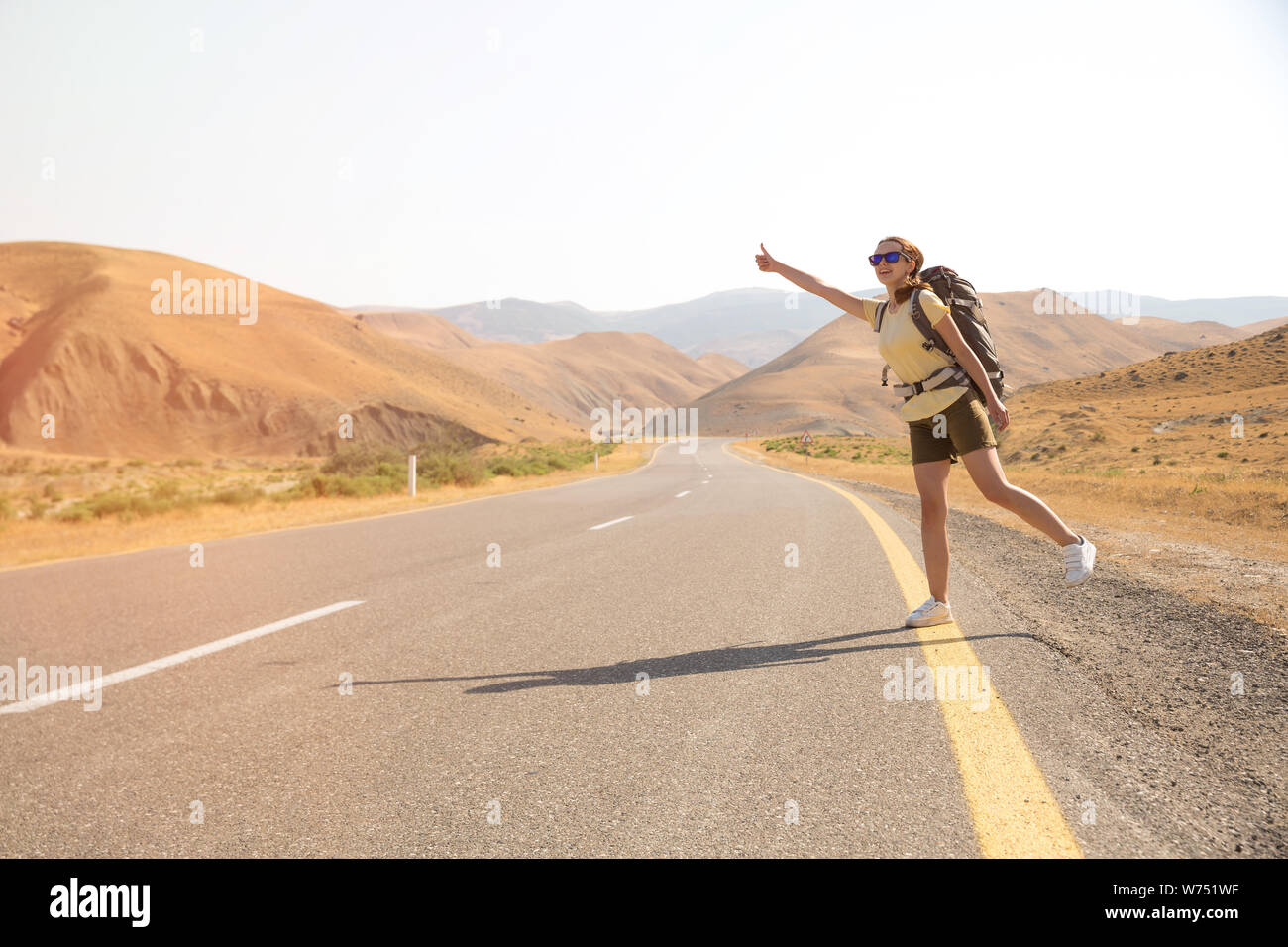 Auto-stoppeur femme voyageur sur la route dans le coucher du soleil. Girl traveler randonneur sur la route. Vacances d'été. La liberté. Banque D'Images