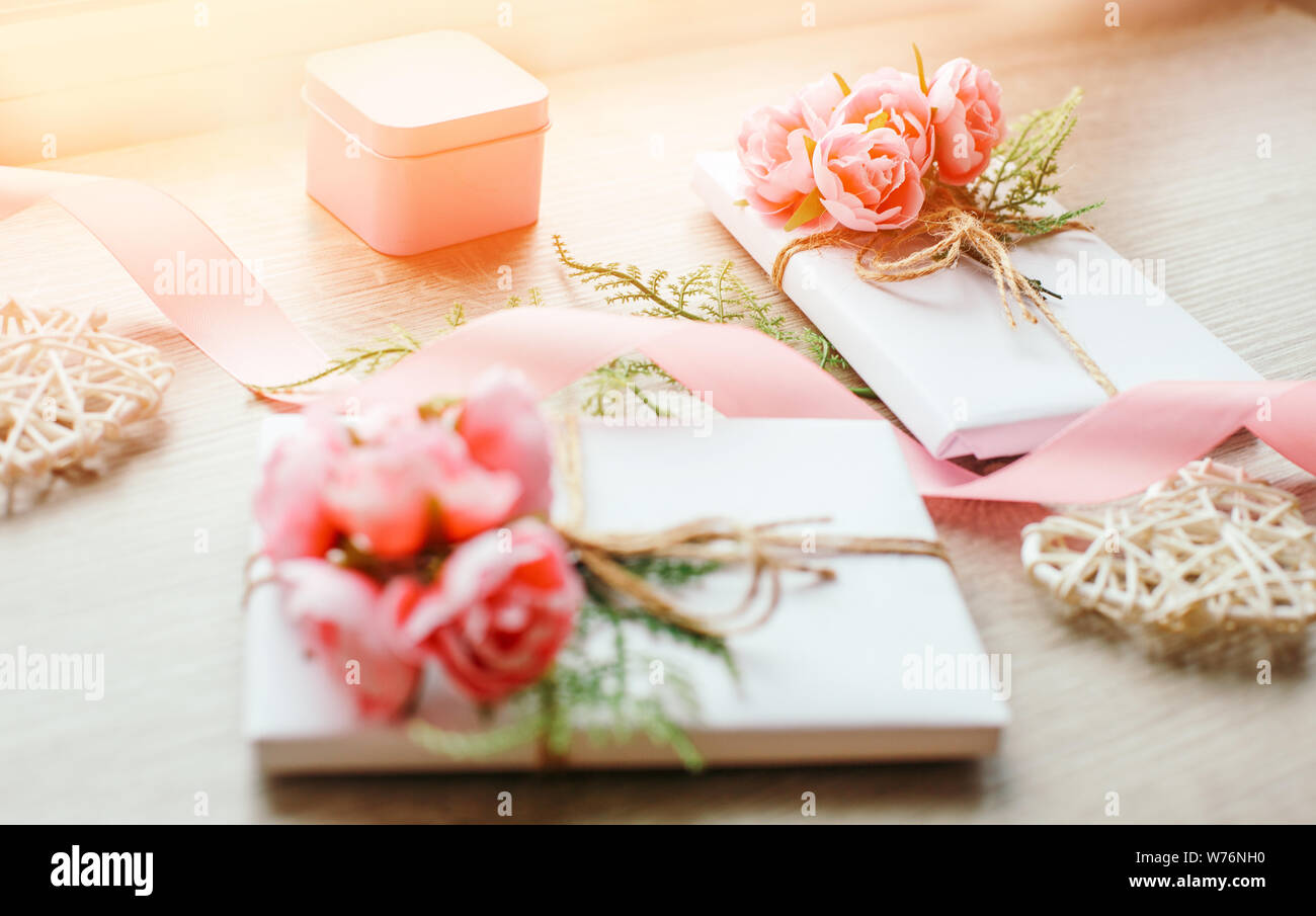 Boîtes-cadeaux enveloppées de papier blanc artisanal simple et d'un bouquet de roses et d'une branche verte. Petite boîte-cadeau rose et ruban rose. Banque D'Images