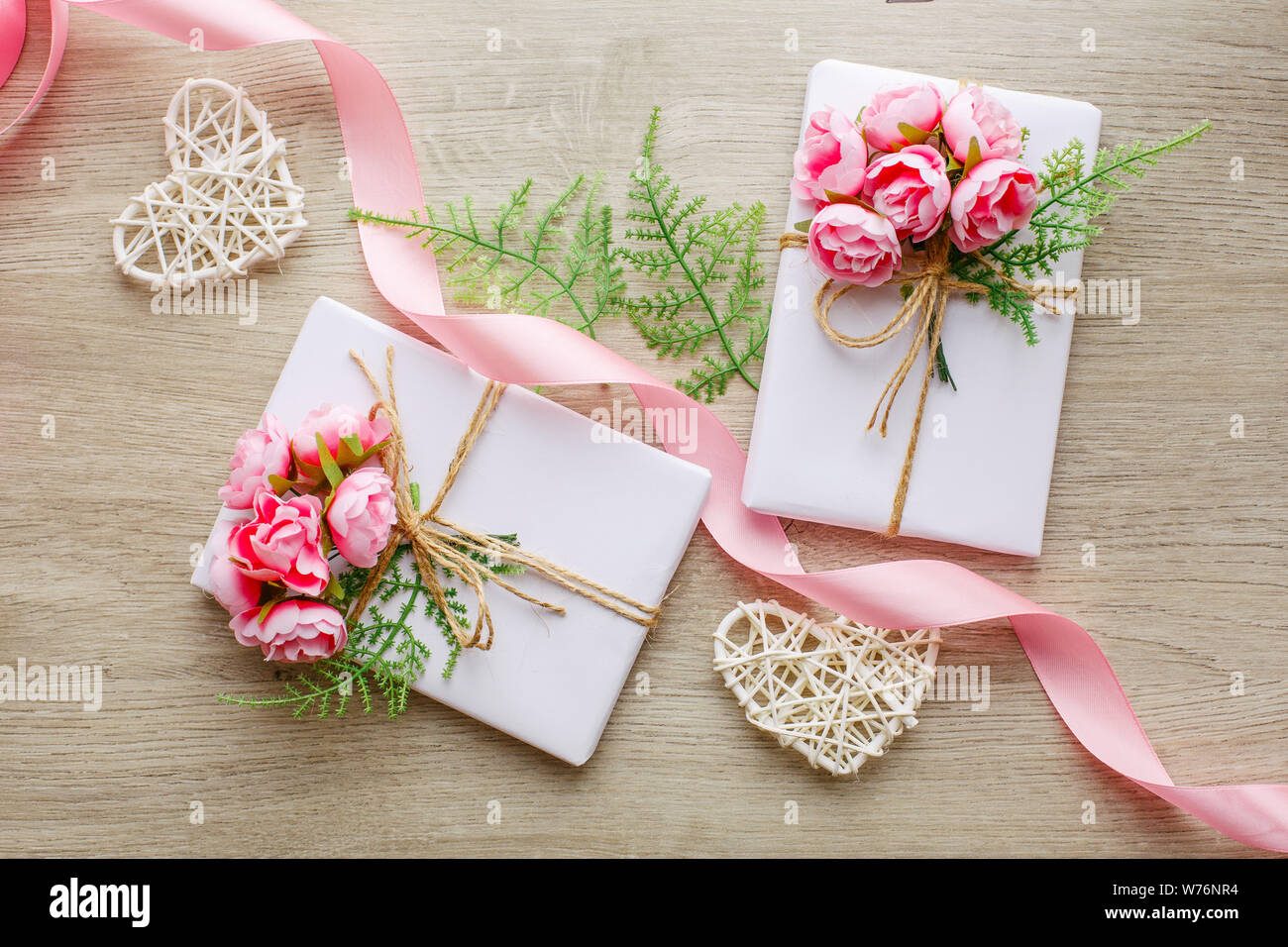 Composition avec boîtes cadeau décorées de branches vertes, de roses, de coeurs en bois et de ruban rose satiné. Banque D'Images