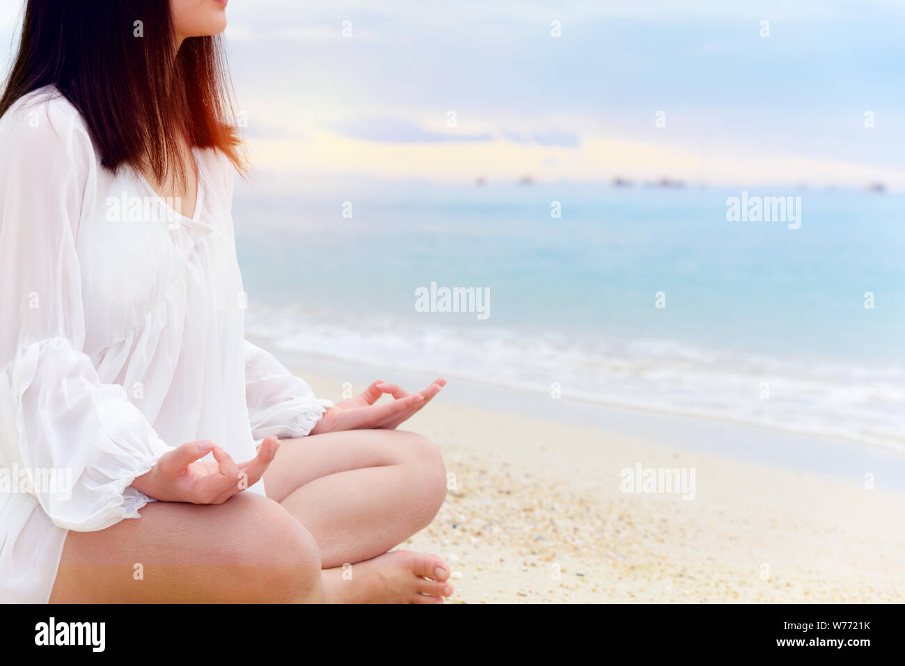 Jeune femme asiatique pratiquer le yoga sur la plage près de la mer, en vertu de la lumière du soleil au lever du soleil, la relaxation pour la santé dans le milieu de la nature avec bonheur et de p Banque D'Images