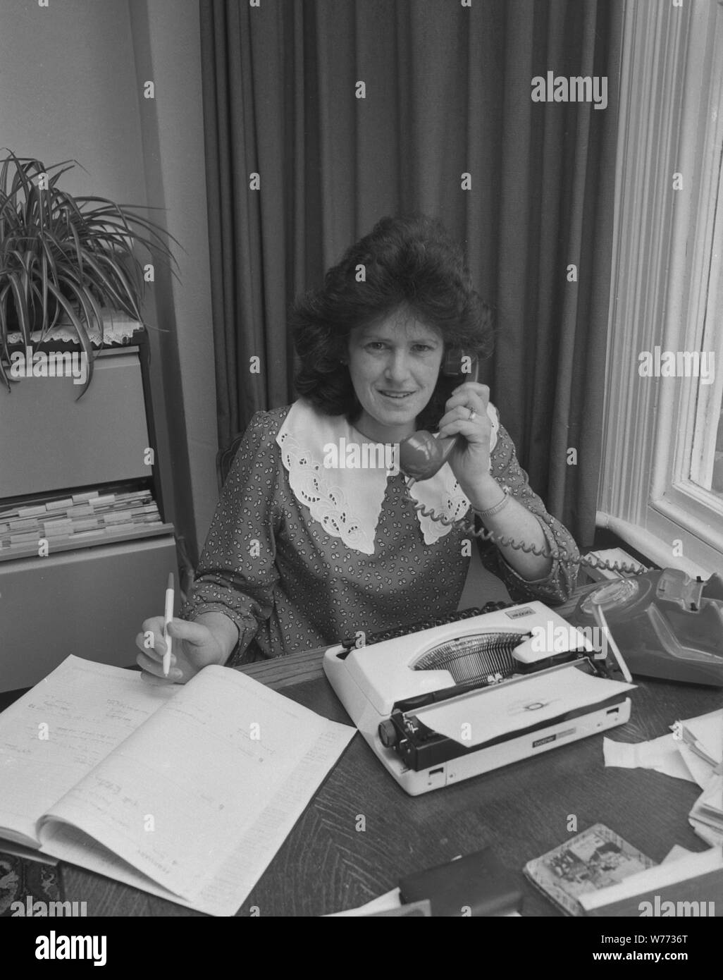 Années 1980, secrétaire de bureau au téléphone, stylo à la main, avec journal intime et machine à écrire de l'époque sur son bureau, Angleterre, Royaume-Uni. Banque D'Images