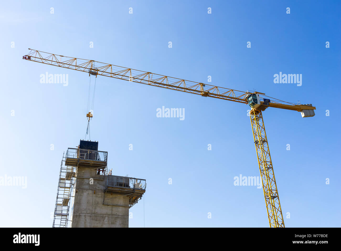 Jusqu'à la grue jaune à un matériau de tomber sur un bâtiment en construction ou de leur lieu de travail. Fond de Ciel bleu ensoleillé. Banque D'Images