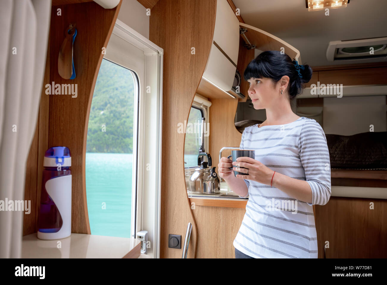 Femme à l'intérieur d'un camping-car RV camping avec une tasse de café en regardant la nature. Banque D'Images