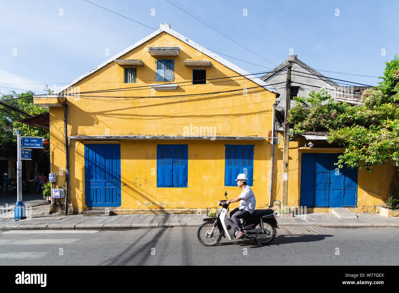 Hoi An, Vietnam - Juin 2019 : man riding scooter vintage à côté de maison coloré dans la vieille ville Banque D'Images