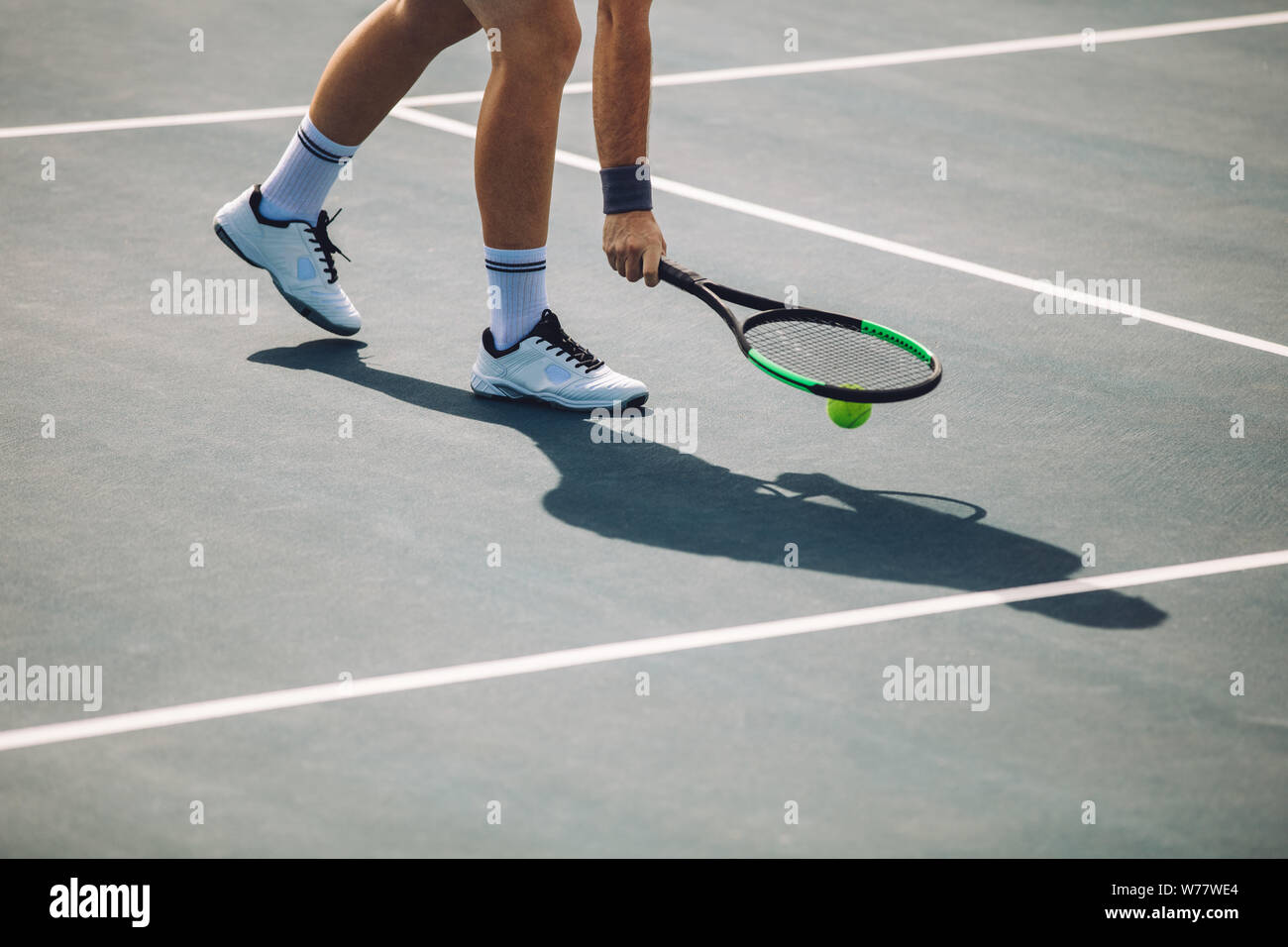 Cropped shot de sportif sur tennis picking la balle avec la raquette. Joueur de tennis masculin ramasser la balle sur surface dure. Banque D'Images