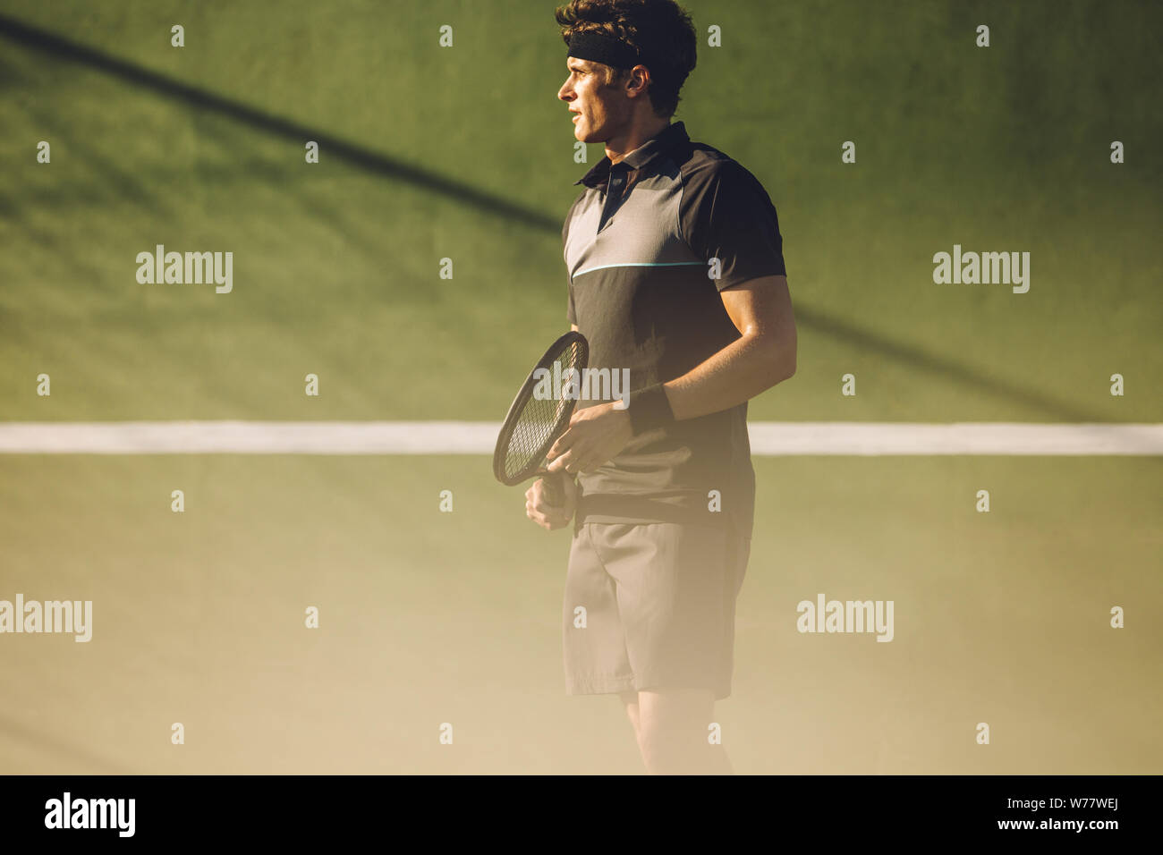 Fit jeune homme en vêtements de sport avec une raquette debout sur un court de tennis. joueur de tennis jouant sur un terrain dur de club. Banque D'Images
