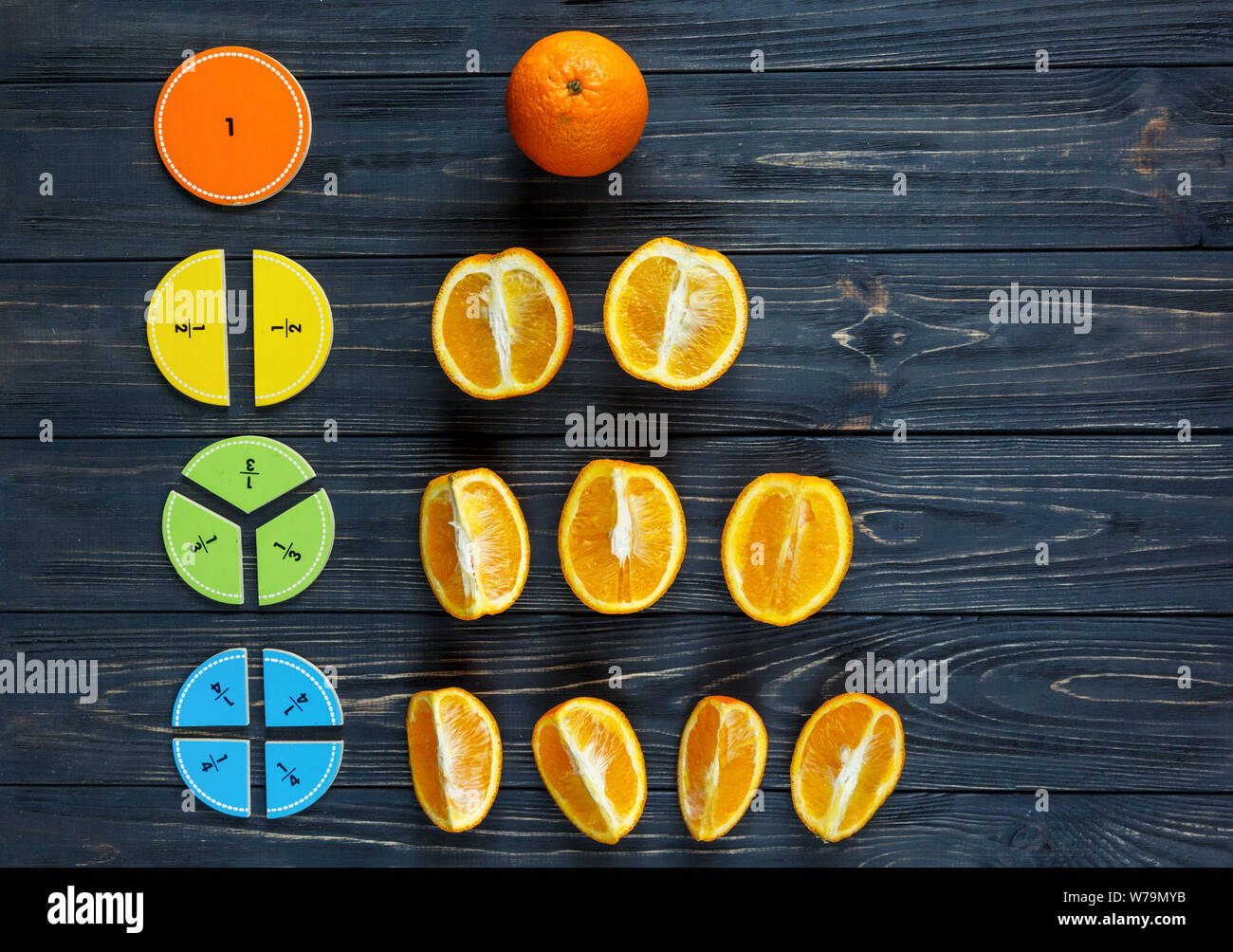 Сolorful fractions mathématiques et des oranges comme un échantillon sur fond de bois sombre ou d'une table. Intéressante de création de funny math pour les enfants. L'éducation, de retour à schoo Banque D'Images