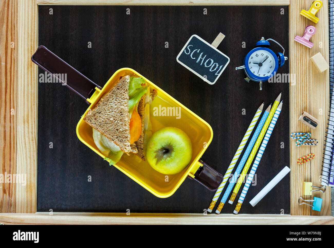 Jaune de l'école boîte à lunch avec sandwich, pomme verte, horloge sur tableau. Une saine alimentation à l'école. Retour à l'école. Mise à plat, vue du dessus. Banque D'Images