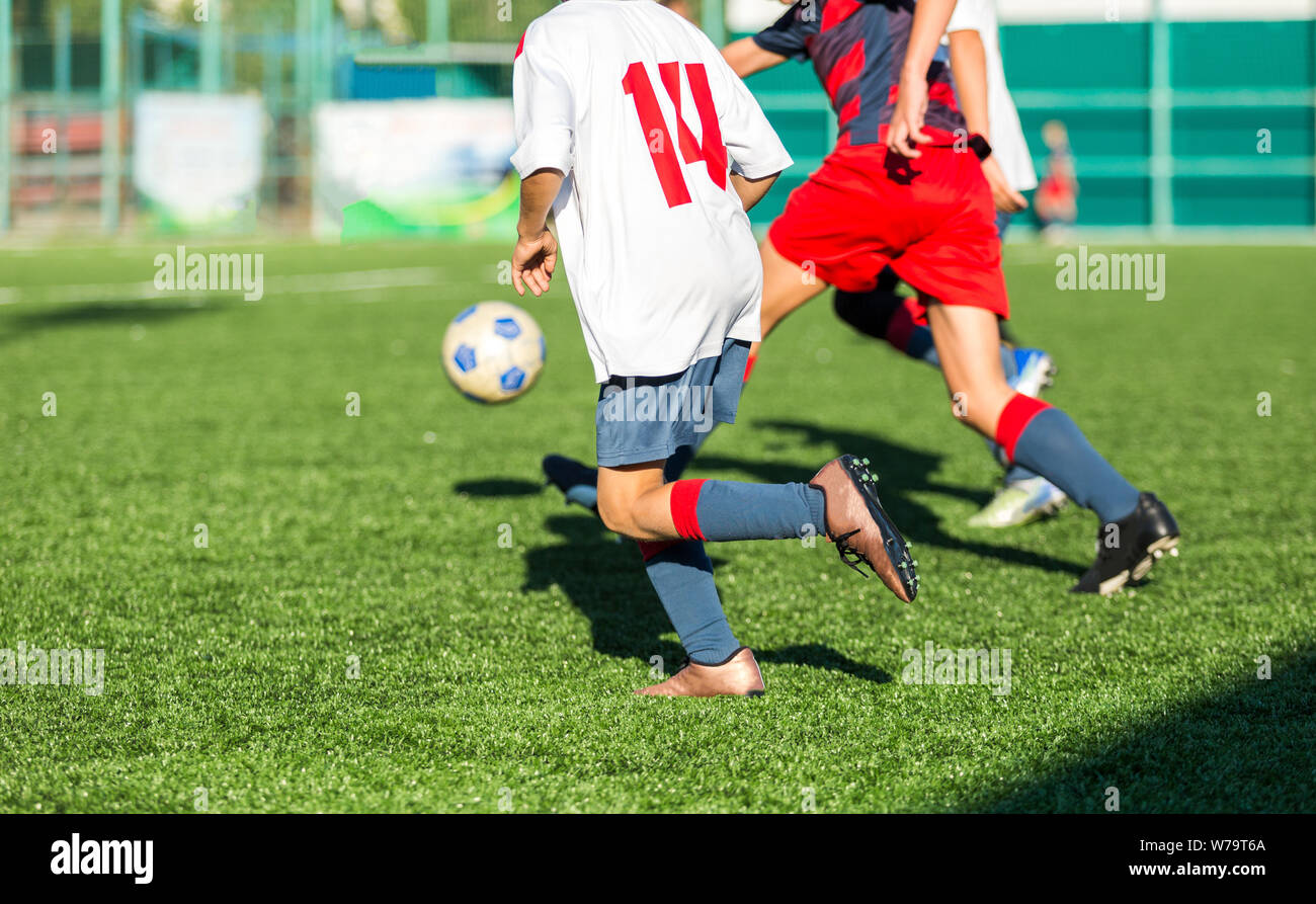 Les garçons en rouge et bleu joue au football sur terrain de sport, dribbles ballon. Les jeunes joueurs de soccer avec boule sur l'herbe verte. La formation, football Banque D'Images