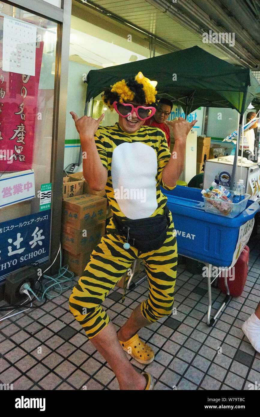 Homme habillé en jaune vif-tigre body impression coeur, lunettes de soleil, et un paquet de fanny pose avec shakas à l'Akita Kanto Matsuri festival en 2016. Banque D'Images