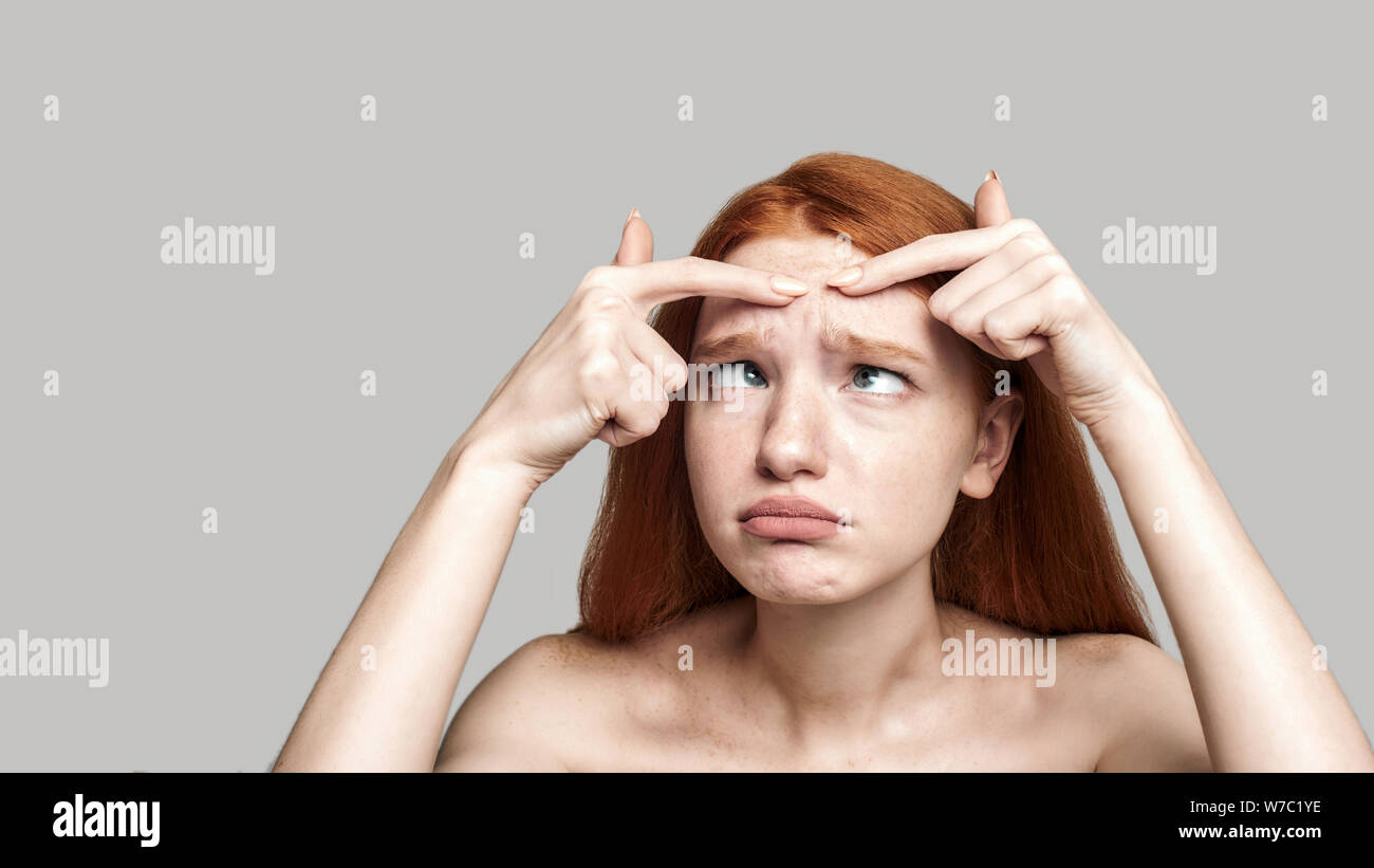 Portrait de jeune femme rousse inquiète sur son visage alors qu'il se tenait à l'arrière-plan gris. Soins de la peau Banque D'Images