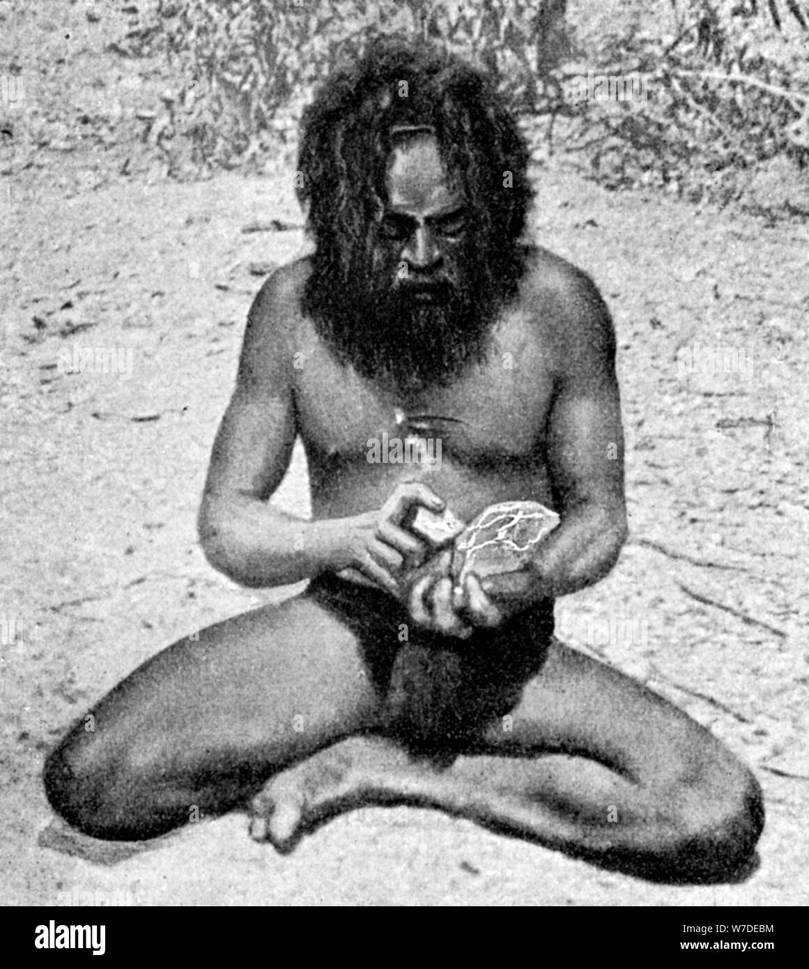 Un homme de la tribu Warramunga faisant une tête de hache de pierre, de l'Australie, 1922.Artiste : Spencer et Gillen Banque D'Images