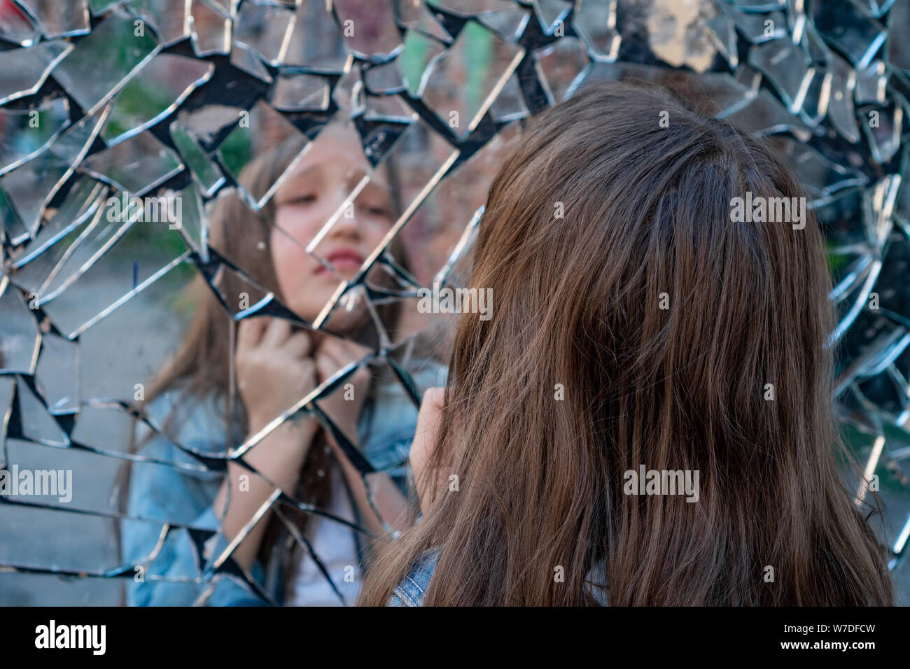 Jeune fille lycéenne cherche dans un miroir cassé et souffre et montre sur la gorge. Banque D'Images