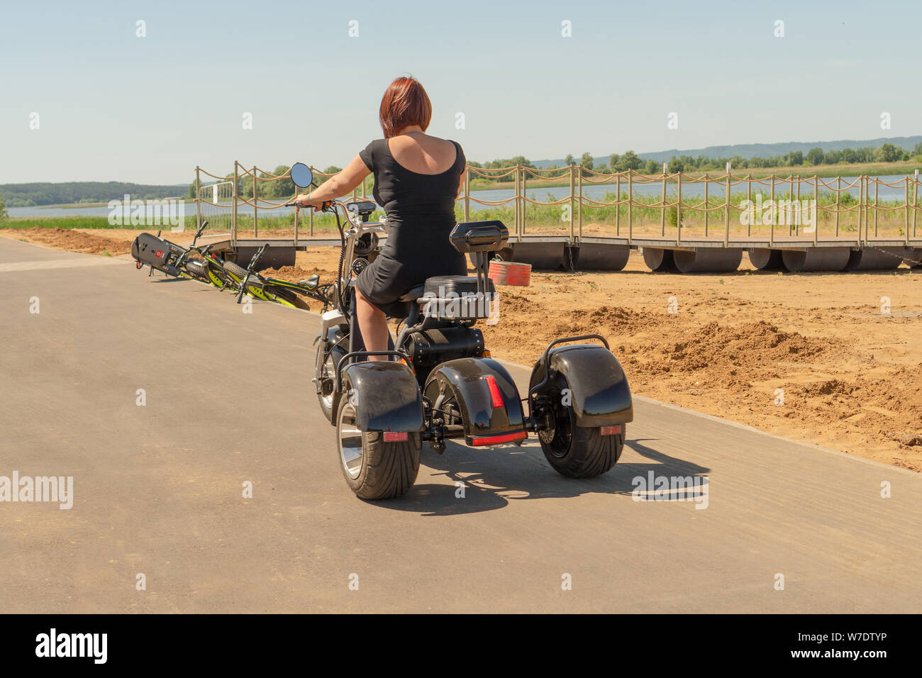 La Russie, Bolgar - Juin 08, 2019 Gali Kol Resort&Spa : Une jeune fille  dans une robe noire aux cheveux rouges conduisant sa moto électrique à  trois roues le long e Photo Stock - Alamy