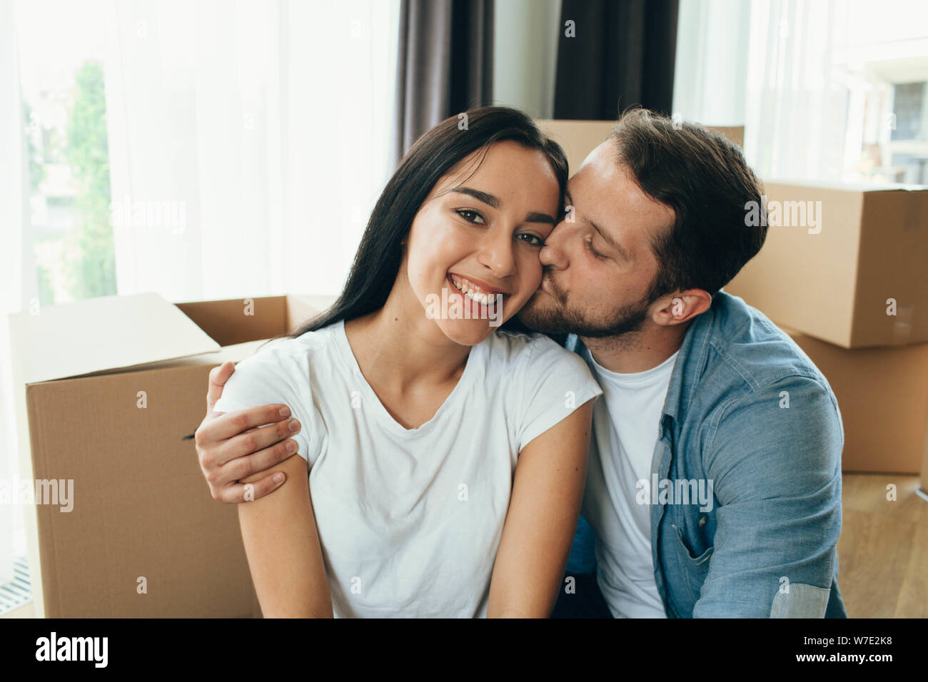 Mixed Race couple heureux se déplaçant à une nouvelle maison. Man and Woman hugging et assis sur le sol près de boîtes de carton Banque D'Images