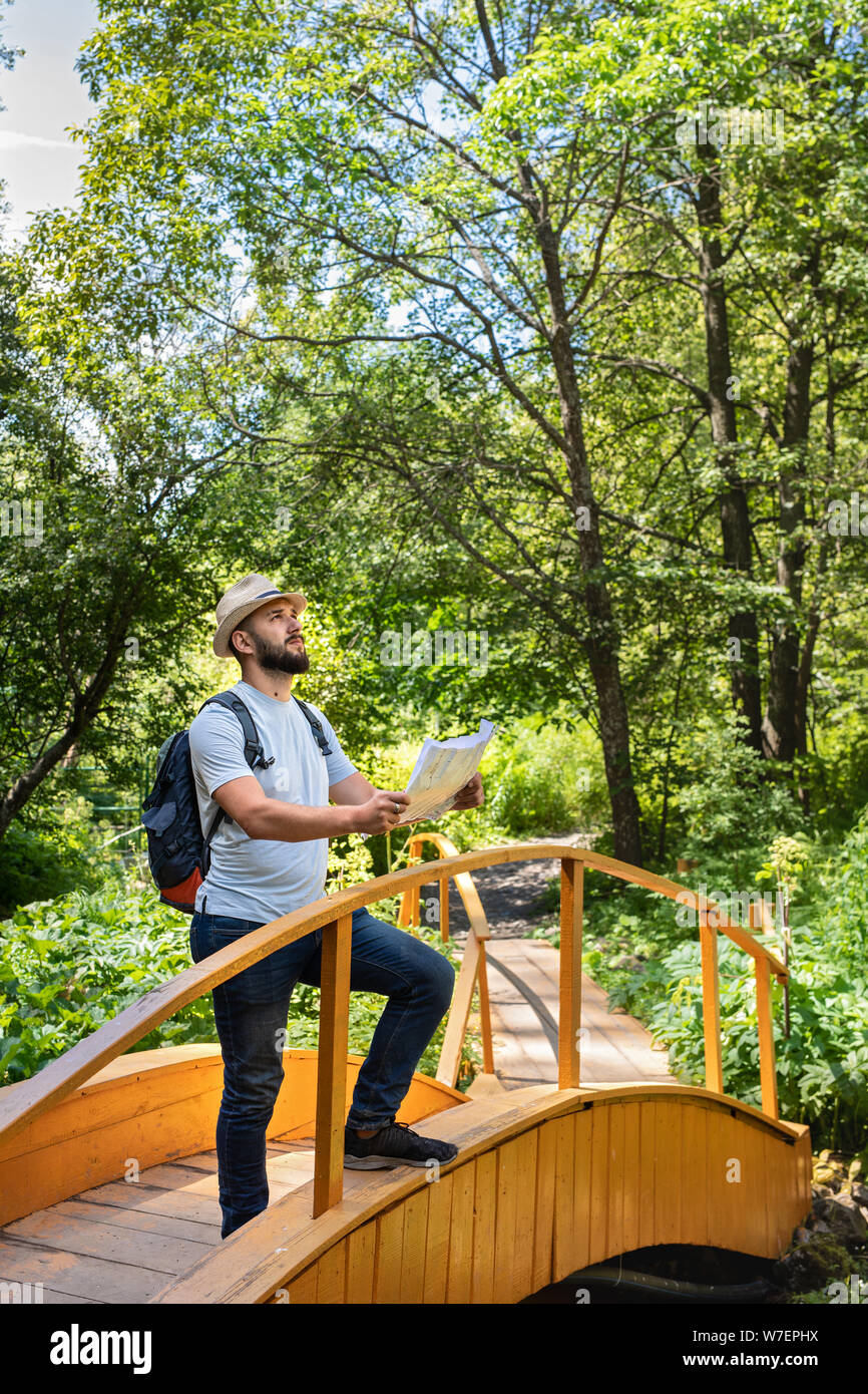 Les jeunes phoques barbus guy millénaire un voyageur dans un chapeau avec un sac à dos se tient sur un pont en bois à la découverte de la région et détermine le chemin sur la carte Banque D'Images