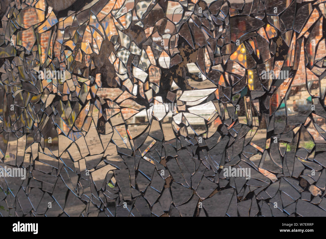 Mur de ciment fissuré avec mosaic sales fabriqués à partir de morceaux de miroir brisé avec distorsion de la réflexion en eux. Résumé La réflexion dans les éclats de miroir. Rough Banque D'Images